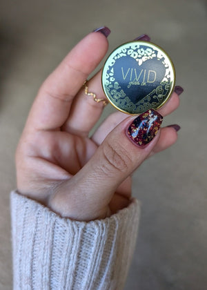 Hand holding a dip powder jar with 'Vivid' branding against a neutral background