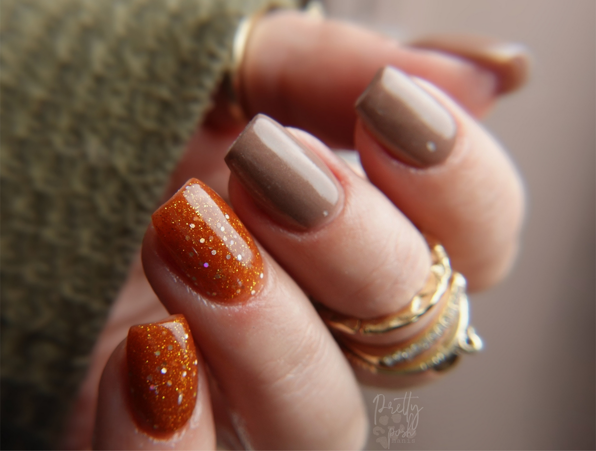 Close-up of a hand with brown and orange glittery nail dip powder on a blurred background
