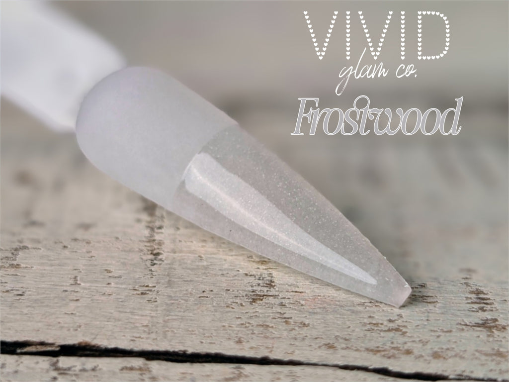 Clear nail art brush tip on a wooden surface with 'Vivid Glam Co. Frostwood' text.